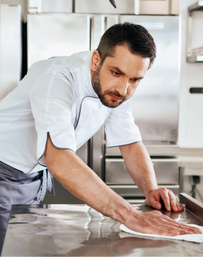 Mann putzt Arbeitsfläche in Großküche
