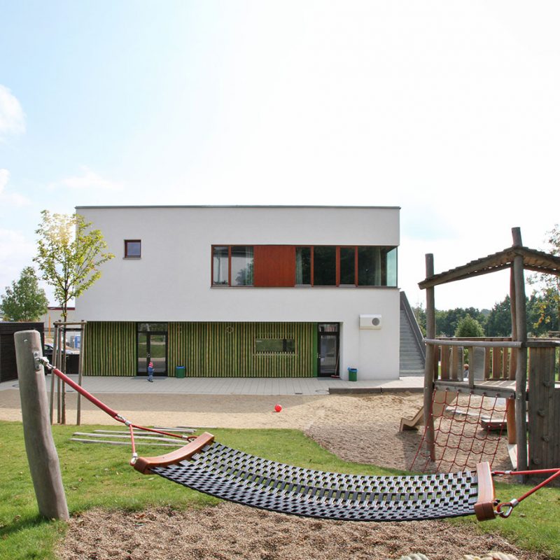 Modernes Kita Gebäude mit Spielplatz und Hängematte