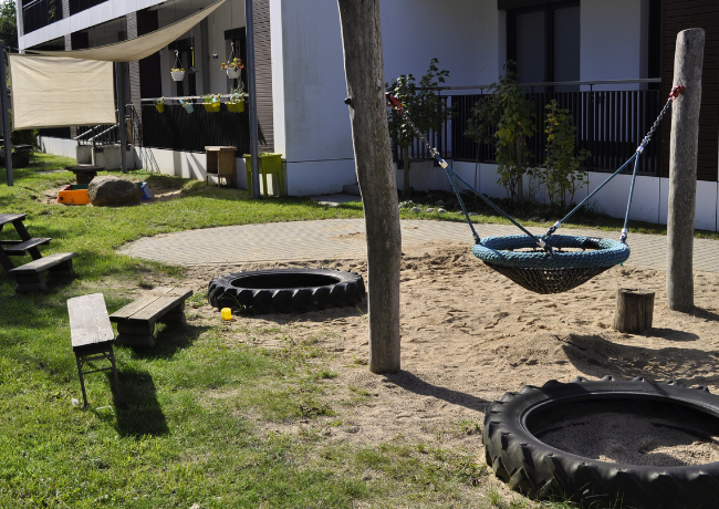 Kindergartenaußengelände mit Schaukel-Korb und großen Reifen im Sand